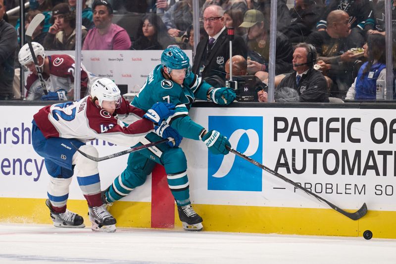 Oct 20, 2024; San Jose, California, USA; San Jose Sharks center Nico Sturm (7) extends for the puck along the boards against Colorado Avalanche defenseman Josh Manson (42) during the second period at SAP Center at San Jose. Mandatory Credit: Robert Edwards-Imagn Images