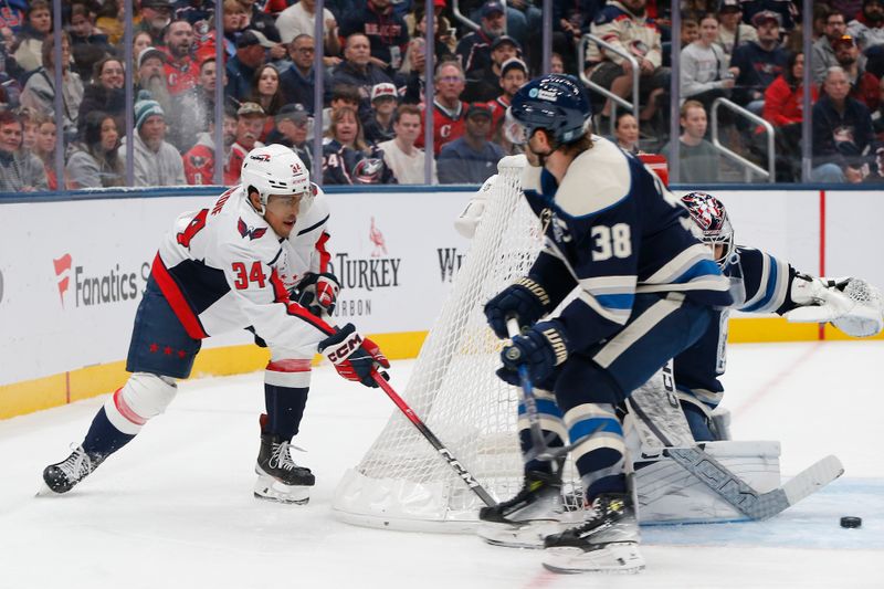 Oct 24, 2025; Columbus, Ohio, USA; Washington Capitals right wing Justin Sourdif (34) passes the puck as Columbus Blue Jackets center Boone Jenner (38) defends during the first period at Nationwide Arena. Mandatory Credit: Russell LaBounty-Imagn Images