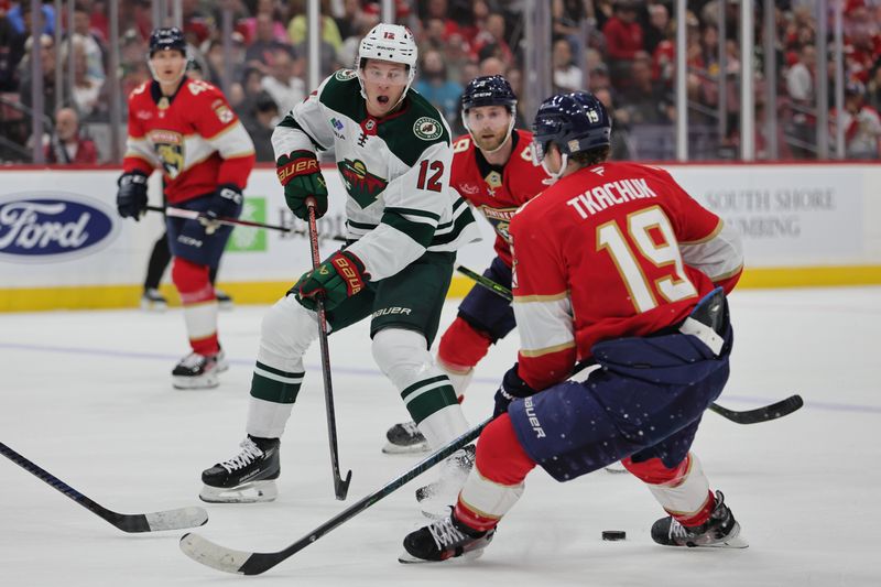 Oct 22, 2024; Sunrise, Florida, USA; Minnesota Wild left wing Matt Boldy (12) moves the puck as Florida Panthers left wing Matthew Tkachuk (19) defends during the first period at Amerant Bank Arena. Mandatory Credit: Sam Navarro-Imagn Images