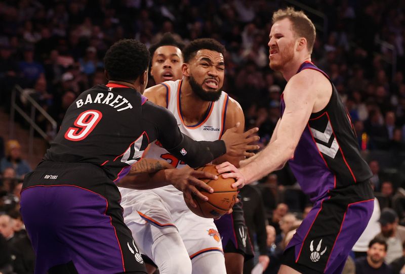 NEW YORK, NEW YORK - JANUARY 08:  Karl-Anthony Towns #32 of the New York Knicks is fouled by Jakob Poeltl #19 of the Toronto Raptors and RJ Barrett #9 of the Toronto Raptors during their game at Madison Square Garden on January 08, 2025 in New York City.   User expressly acknowledges and agrees that, by downloading and or using this photograph, User is consenting to the terms and conditions of the Getty Images License Agreement.  (Photo by Al Bello/Getty Images)