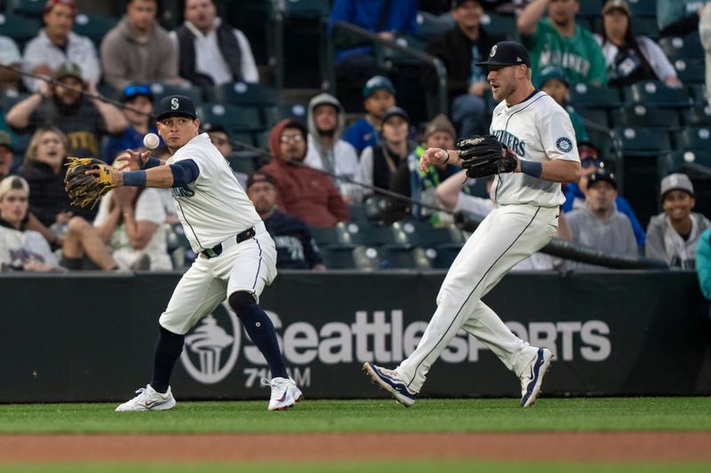 May 13, 2024; Seattle, Washington, USA; Seattle Mariners third baseman Luis Urias (16) loses the ball as he attempts to throw the ball to second base during the seventh inning against the Kansas City Royals at T-Mobile Park. At right is Seattle Mariners left fielder Luke Raley (20). Mandatory Credit: Stephen Brashear-USA TODAY Sports