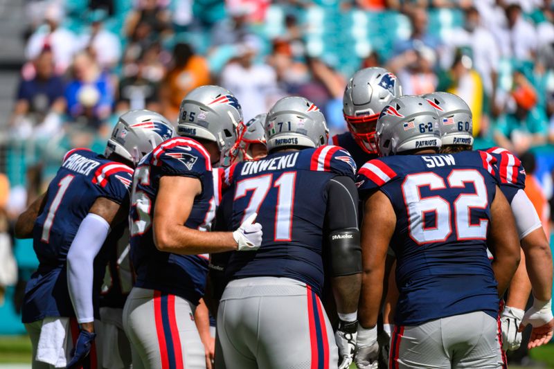 New England Patriots wide receiver DeVante Parker (1), tight end Hunter Henry (85), offensive lineman Mike Onwenu (71) and offensive lineman Sidy Sow (62) in the huddle during an NFL football game against the Miami Dolphins, Sunday, Oct. 29, 2023, in Miami Gardens, Fla. (AP Photo/Doug Murray)