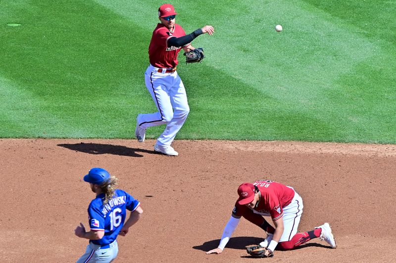 Mar 8, 2023; Salt River Pima-Maricopa, Arizona, USA; Arizona Diamondbacks shortstop Nick Ahmed (13) throws to first base as third baseman Josh Rojas (10) ducks and Texas Rangers center fielder Travis Jankowski (16) looks on in the third inning  during a Spring Training game at Salt River Fields at Talking Stick. Mandatory Credit: Matt Kartozian-USA TODAY Sports