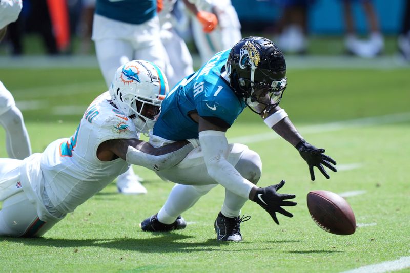 Miami Dolphins safety Jevon Holland (8) grabs Jacksonville Jaguars running back Travis Etienne Jr. (1) as he fumbles the ball during the second half of an NFL football game, Sunday, Sept. 8, 2024, in Miami Gardens, Fla. (AP Photo/Wilfredo Lee)