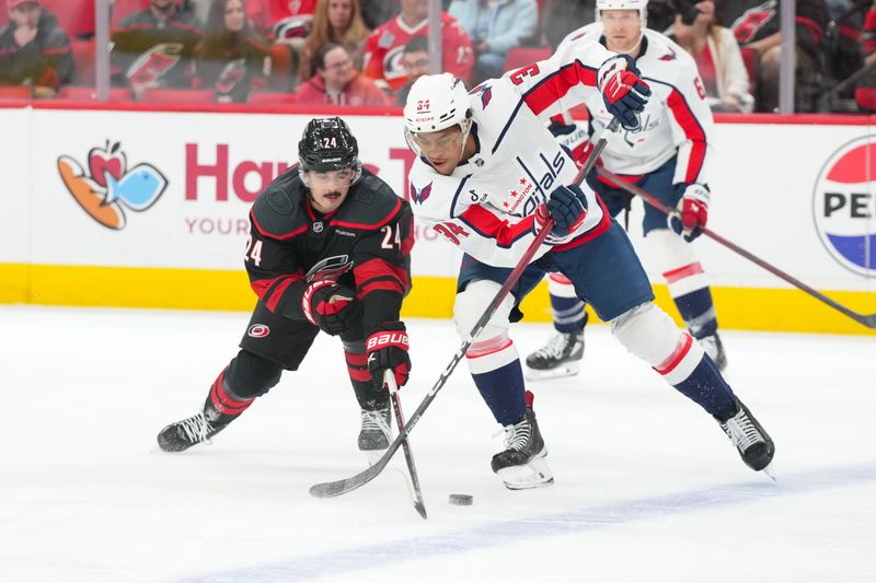 Nov 11, 2025; Raleigh, North Carolina, USA;  Carolina Hurricanes center Seth Jarvis (24) pokes the puck away from Washington Capitals right wing Justin Sourdif (34) during the first period at Lenovo Center. Mandatory Credit: James Guillory-Imagn Images