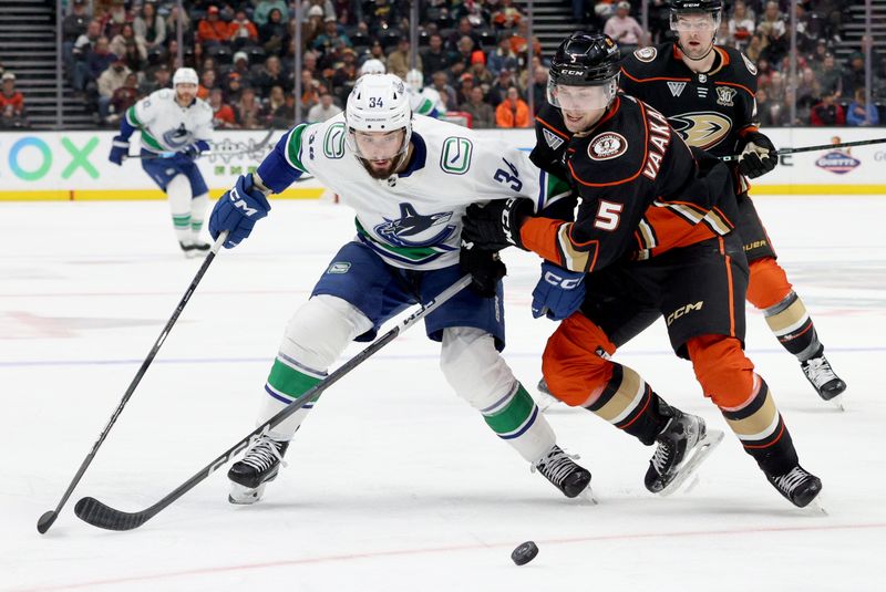 Mar 3, 2024; Anaheim, California, USA; Vancouver Canucks left wing Phillip Di Giuseppe (34) and Anaheim Ducks defenseman Urho Vaakanainen (5) fight for the puck during the third period at Honda Center. Mandatory Credit: Jason Parkhurst-USA TODAY Sports