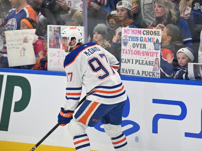 Nov 16, 2024; Toronto, Ontario, CAN;   Edmonton Oilers forward Connor McDavid (97) skates past a sign held by a fan referencing the nearby Taylor Swift concerts as he warms up before playing the Toronto Maple Leafs at Scotiabank Arena. Mandatory Credit: Dan Hamilton-Imagn Images