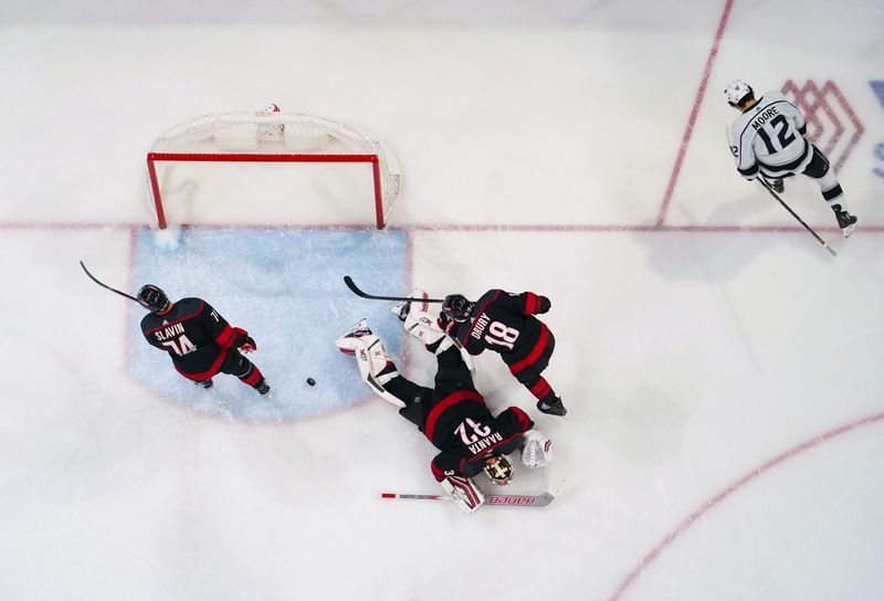 Jan 15, 2024; Raleigh, North Carolina, USA;  Los Angeles Kings left wing Trevor Moore (12) scores a goal past Carolina Hurricanes goaltender Antti Raanta (32) center Jack Drury (18) and defenseman Jaccob Slavin (74) during the first period at PNC Arena. Mandatory Credit: James Guillory-USA TODAY Sports