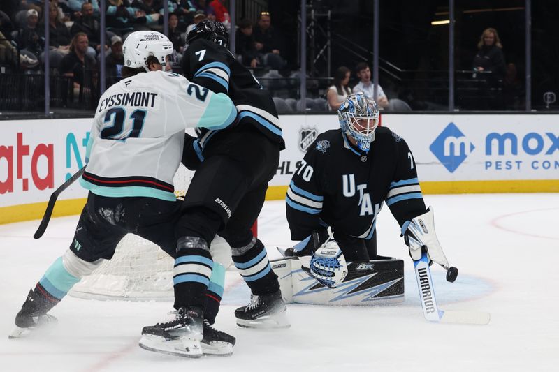 Apr 8, 2025; Salt Lake City, Utah, USA; Utah Hockey Club goaltender Karel Vejmelka (70) blocks a shot as Seattle Kraken center Michael Eyssimont (21) and Utah Hockey Club defenseman Michael Kesselring (7) battle during the third period at Delta Center. Mandatory Credit: Rob Gray-Imagn Images