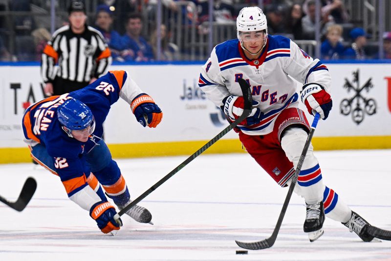 Feb 25, 2025; Elmont, New York, USA;  New York Rangers defenseman Braden Schneider (4) skates the puck against New York Islanders center Kyle MacLean (32) during the third period at UBS Arena. Mandatory Credit: Dennis Schneidler-Imagn Images