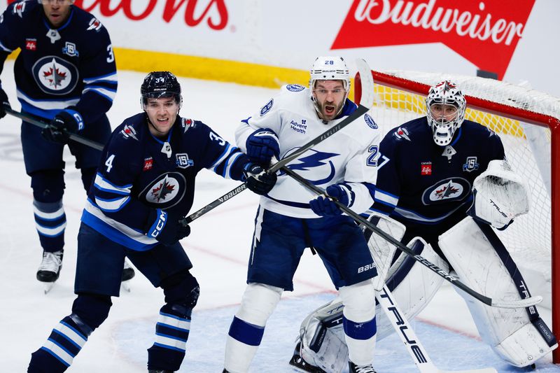 Mar 5, 2026; Winnipeg, Manitoba, CAN;  Winnipeg Jets defenseman Ville Heinola (34) jostles for position with Tampa Bay Lightning forward Zemgus Gingensons (28) in front of Winnipeg Jets goalie Connor Hellebuyck (37) during the third period at Canada Life Centre. Mandatory Credit: Terrence Lee-Imagn Images