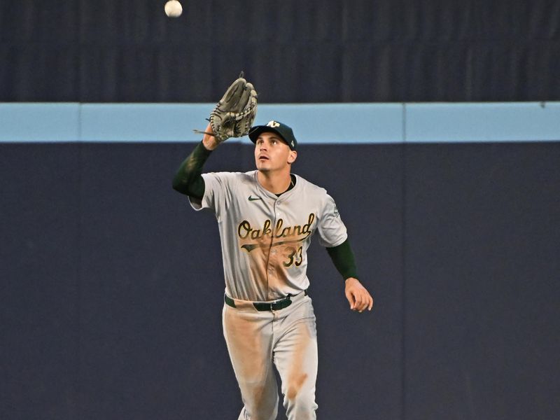 Aug 11, 2024; Toronto, Ontario, CAN; Oakland Athletics centre field JJ Bleday (33) fields a fly ball from Toronto Blue Jays short stop Ernie Clement (28) in the seventh inning at Rogers Centre. Mandatory Credit: Gerry Angus-USA TODAY Sports