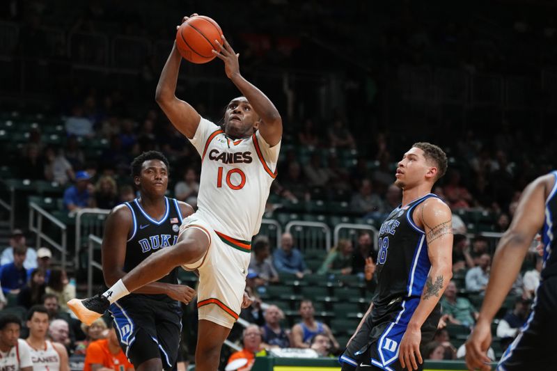 Feb 25, 2025; Coral Gables, Florida, USA;  Miami (Fl) Hurricanes guard Paul Djobet (10) splits the defense of Duke Blue Devils center Patrick Ngongba II (21) and forward Mason Gillis (18) during the second half at Watsco Center. Mandatory Credit: Jim Rassol-Imagn Images