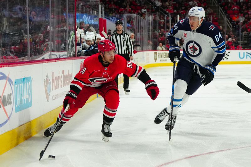 Mar 2, 2024; Raleigh, North Carolina, USA; Carolina Hurricanes left wing Michael Bunting (58) skates with the puck past Winnipeg Jets defenseman Logan Stanley (64) during the first period at PNC Arena. Mandatory Credit: James Guillory-USA TODAY Sports