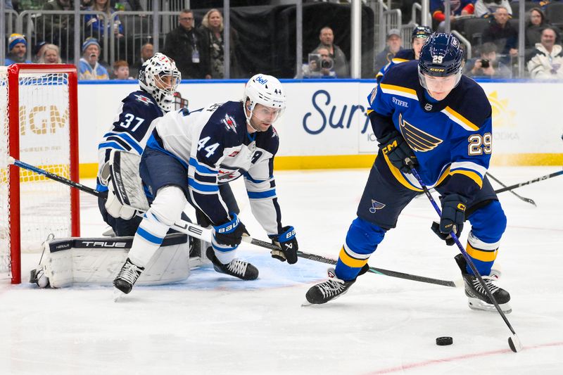 Dec 17, 2025; St. Louis, Missouri, USA; St. Louis Blues right wing Jonatan Berggren (29) controls the puck as Winnipeg Jets defenseman Josh Morrissey (44) and goaltender Connor Hellebuyck (37) defend the net during the second period at Enterprise Center. Mandatory Credit: Jeff Curry-Imagn Images