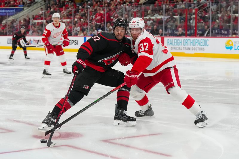 Dec 27, 2025; Raleigh, North Carolina, USA;  Carolina Hurricanes center Jesperi Kotkaniemi (82) battles over the agents Detroit Red Wings left wing J.T. Compher (37) during the third period at Lenovo Center. Mandatory Credit: James Guillory-Imagn Images