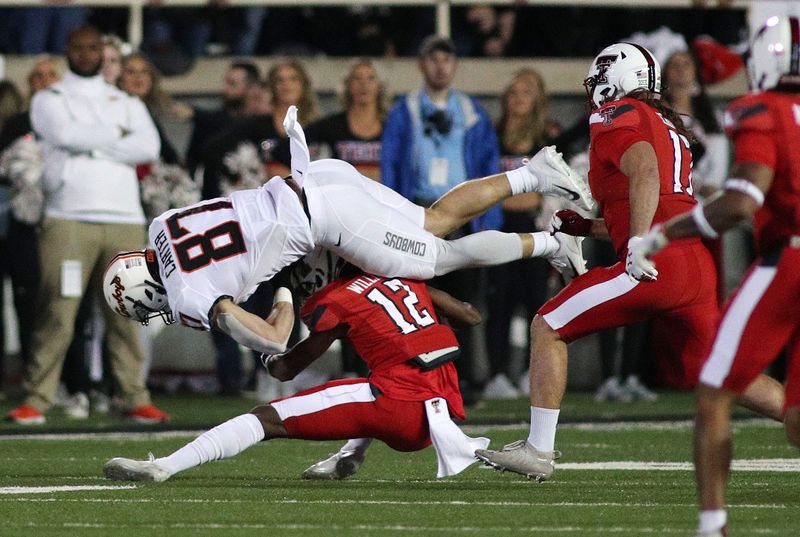 Nov 20, 2021; Lubbock, Texas, USA;  Oklahoma State Cowboys wide receiver Logan Carter (87) is tripped up by Texas Tech Red Raiders defensive corner back Rayshad Williams (12) in the first half at Jones AT&T Stadium. Mandatory Credit: Michael C. Johnson-USA TODAY Sports