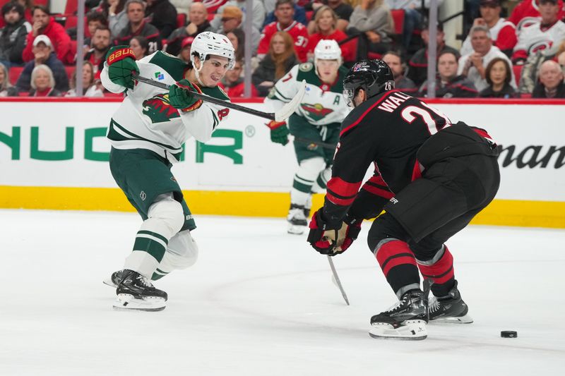 Nov 6, 2025; Raleigh, North Carolina, USA;  Minnesota Wild defenseman Zeev Buium (8) gets the shot away against Carolina Hurricanes defenseman Sean Walker (26) during the second period at Lenovo Center. Mandatory Credit: James Guillory-Imagn Images