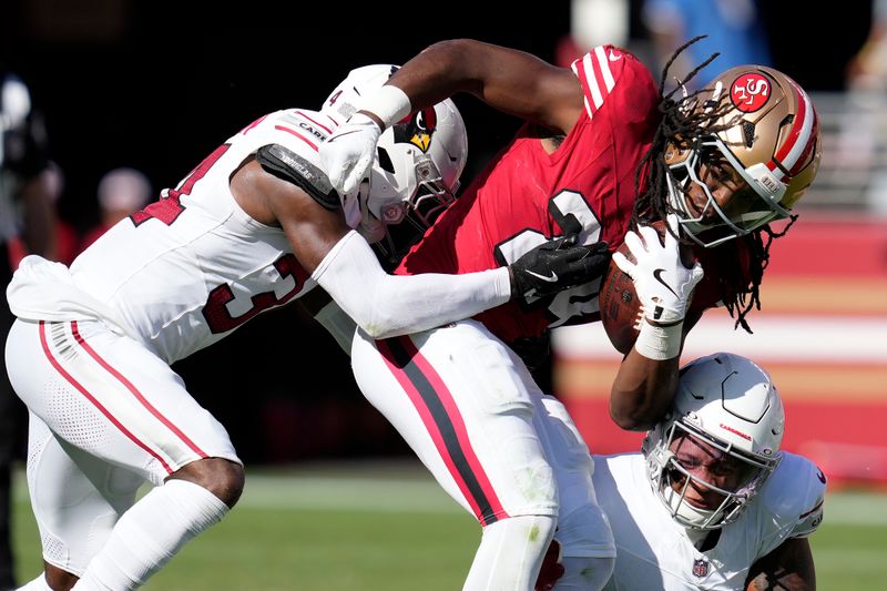 San Francisco 49ers running back Jordan Mason, middle, runs against Arizona Cardinals safety Jalen Thompson, left, and linebacker Jesse Luketa during the second half of an NFL football game in Santa Clara, Calif., Sunday, Oct. 6, 2024. (AP Photo/Godofredo A. Vásquez)