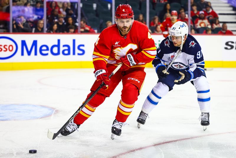 Oct 4, 2024; Calgary, Alberta, CAN; Calgary Flames defenseman Rasmus Andersson (4) controls the puck against Winnipeg Jets center Cole Perfetti (91) during the first period at Scotiabank Saddledome. Mandatory Credit: Sergei Belski-Imagn Images