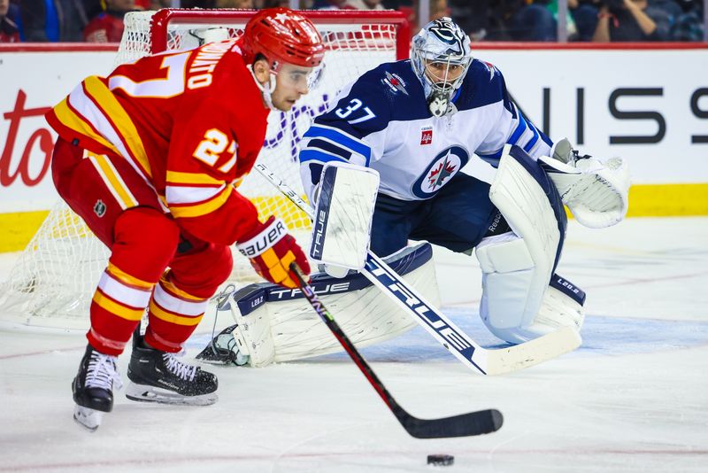 Oct 11, 2023; Calgary, Alberta, CAN; Winnipeg Jets goaltender Connor Hellebuyck (37) guards his net as Calgary Flames right wing Matt Coronato (27) controls the puck during the second period at Scotiabank Saddledome. Mandatory Credit: Sergei Belski-USA TODAY Sports