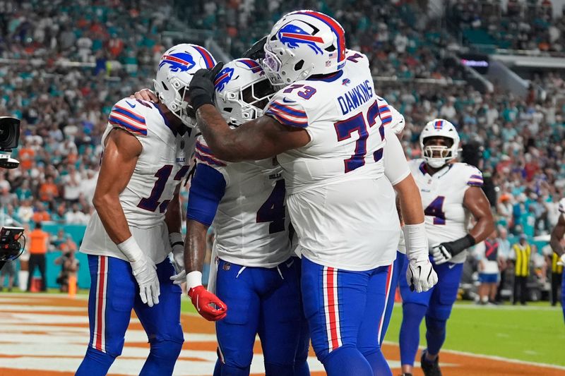 Buffalo Bills running back James Cook (4) is congratulated by offensive tackle Dion Dawkins (73) and wide receiver Mack Hollins (13) after scoring a touchdown during the first half of an NFL football game against the Miami Dolphins, Thursday, Sept. 12, 2024, in Miami Gardens, Fla. (AP Photo/Lynne Sladky)