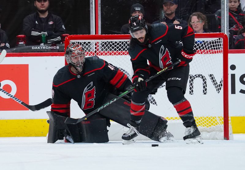 Nov 27, 2024; Raleigh, North Carolina, USA;  Carolina Hurricanes defenseman Jalen Chatfield (5) goes to clear the puck away from in front of goaltender Spencer Martin (41) against the New York Rangers during the first period at Lenovo Center. Mandatory Credit: James Guillory-Imagn Images