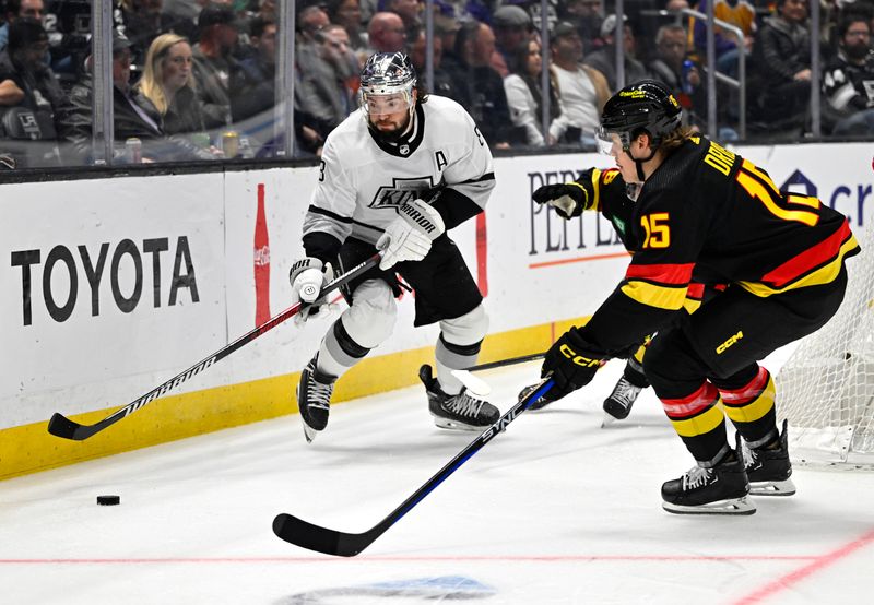 Apr 10, 2023; Los Angeles, California, USA;  Los Angeles Kings defenseman Drew Doughty (8) passes the puck around Vancouver Canucks center Sheldon Dries (15) in the first period at Crypto.com Arena. Mandatory Credit: Jayne Kamin-Oncea-USA TODAY Sports