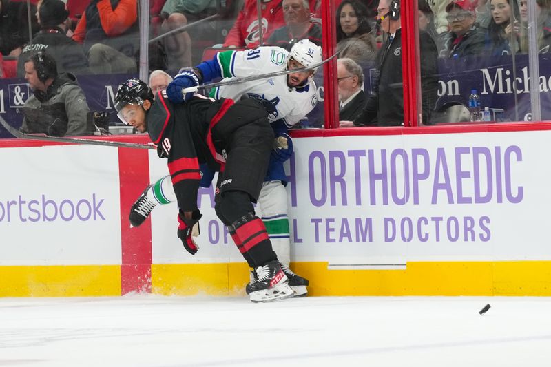 Nov 14, 2025; Raleigh, North Carolina, USA;  Carolina Hurricanes defenseman K'Andre Miller (19) checks Vancouver Canucks left wing Evander Kane (91) during the second period at Lenovo Center. Mandatory Credit: James Guillory-Imagn Images
