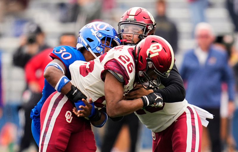 Oct 23, 2021; Lawrence, Kansas, USA; Oklahoma Sooners quarterback Caleb Williams (13) takes the ball from running back Kennedy Brooks (26) as Kansas Jayhawks linebacker Rich Miller (30) defends during the second half at David Booth Kansas Memorial Stadium. Mandatory Credit: Jay Biggerstaff-USA TODAY Sports