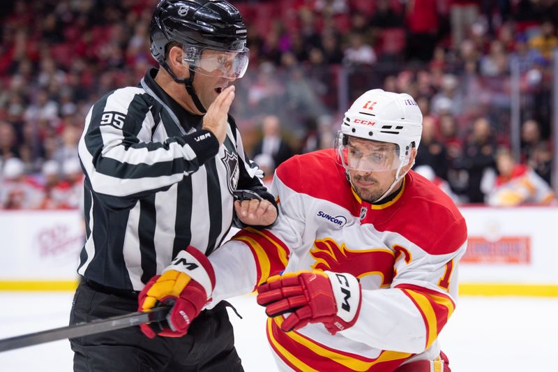 Oct 30, 2025; Ottawa, Ontario, CAN; Calgary Flames center Mikael Backlund (11) is forced to skate around linesperson Jonny Murray (95) as he chases the puck in the first period against the  Ottawa Senators at the Canadian Tire Centre. Mandatory Credit: Marc DesRosiers-IMAGN Images