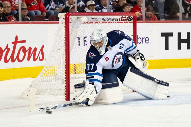 Oct 20, 2025; Calgary, Alberta, CAN; Winnipeg Jets goaltender Connor Hellebuyck (37) reaches to stop a puck during the second period of a game against the Calgary Flames at Scotiabank Saddledome. Mandatory Credit: Brett Holmes-Imagn Images