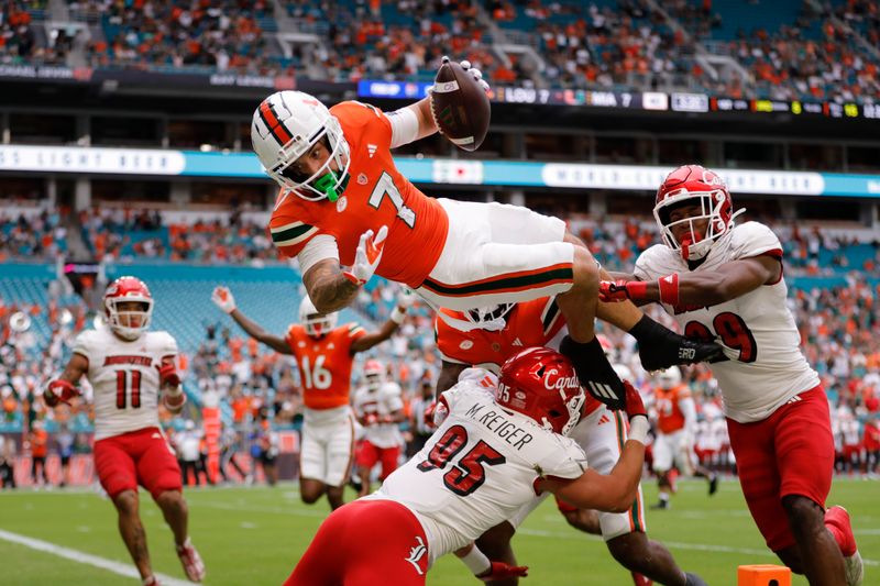 Nov 18, 2023; Miami Gardens, Florida, USA; Miami Hurricanes wide receiver Xavier Restrepo (7) leaps over Louisville Cardinals defensive lineman Mason Reiger (95) for a touchdown during the first quarter at Hard Rock Stadium. Mandatory Credit: Sam Navarro-USA TODAY Sports