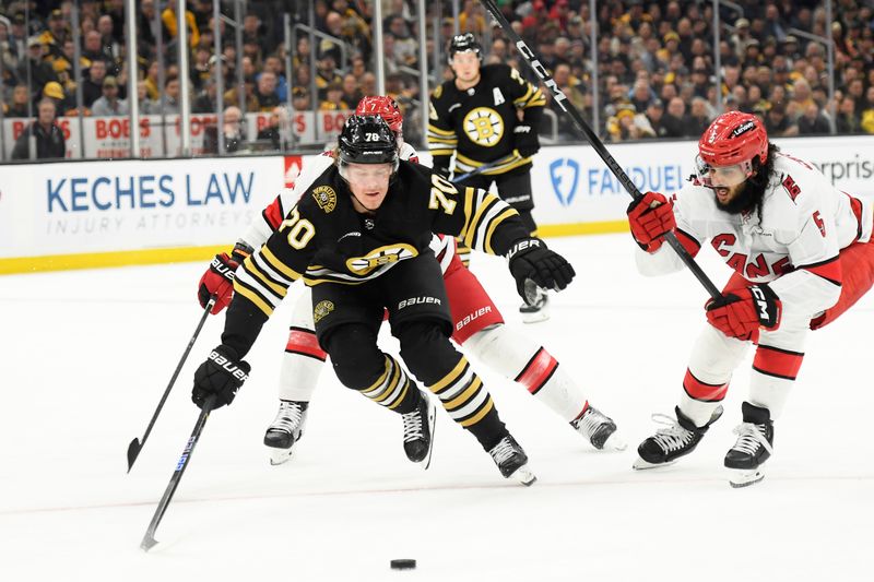 Apr 9, 2024; Boston, Massachusetts, USA; Boston Bruins center Jesper Boqvist (70) reaches for the puck while Carolina Hurricanes defenseman Jalen Chatfield (5) defends during the first period at TD Garden. Mandatory Credit: Bob DeChiara-USA TODAY Sports