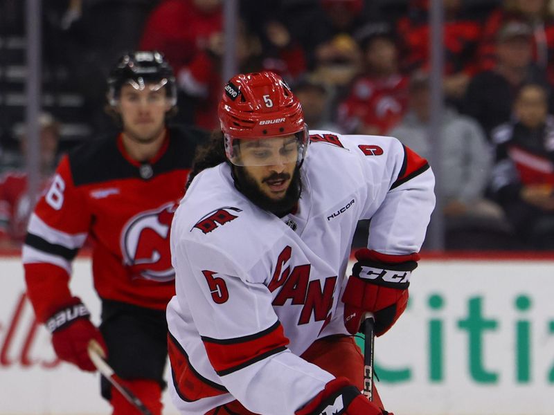 Nov 21, 2024; Newark, New Jersey, USA; Carolina Hurricanes defenseman Jalen Chatfield (5) skates with the puck against the New Jersey Devils during the first period at Prudential Center. Mandatory Credit: Ed Mulholland-Imagn Images