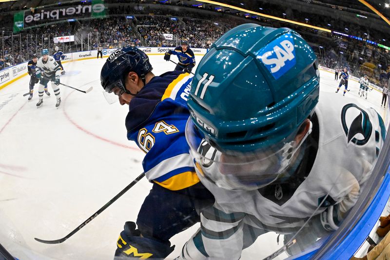 Nov 21, 2024; St. Louis, Missouri, USA;  St. Louis Blues defenseman Corey Schueneman (64) defends against San Jose Sharks center Luke Kunin (11) during the first period at Enterprise Center. Mandatory Credit: Jeff Curry-Imagn Images