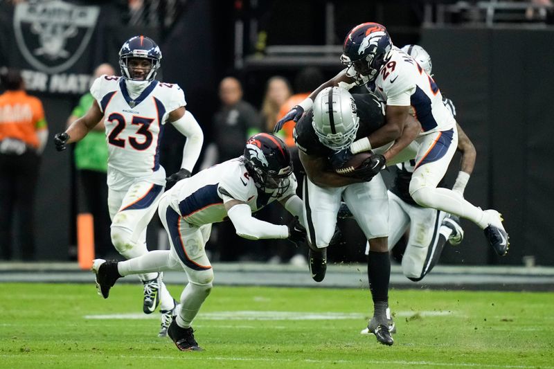 Las Vegas Raiders running back Zamir White, second from right, is tackled by Denver Broncos cornerback Ja'Quan McMillian (29) and safety P.J. Locke during the first half of an NFL football game, Sunday, Jan. 7, 2024 in Las Vegas. (AP Photo/John Locher)