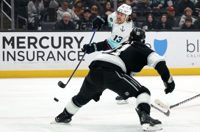 Nov 23, 2024; Los Angeles, California, USA;  Seattle Kraken left wing Brandon Tanev (13) shoots against Los Angeles Kings defenseman Jordan Spence (21) during the first period at Crypto.com Arena. Mandatory Credit: Kiyoshi Mio-Imagn Images