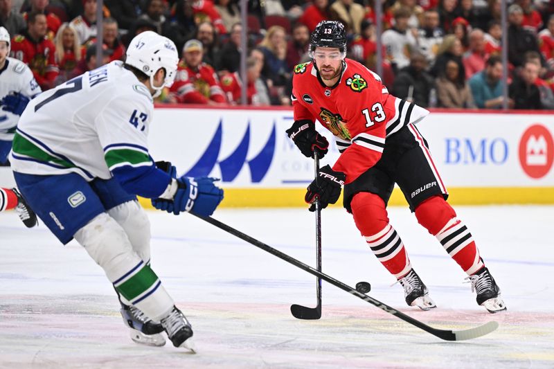 Feb 13, 2024; Chicago, Illinois, USA; Chicago Blackhawks forward Zach Sanford (13) dumps the puck past Vancouver Canucks defenseman Noah Juulsen (47) in the third period at United Center. Mandatory Credit: Jamie Sabau-USA TODAY Sports