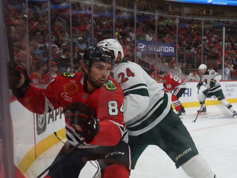 Oct 3, 2025; Chicago, Illinois, USA; Chicago Blackhawks left wing Landon Slaggert (84) and Minnesota Wild defenseman Zach Bogosian (24) battle for control of the puck during the first period at United Center. Mandatory Credit: Talia Sprague-Imagn Images