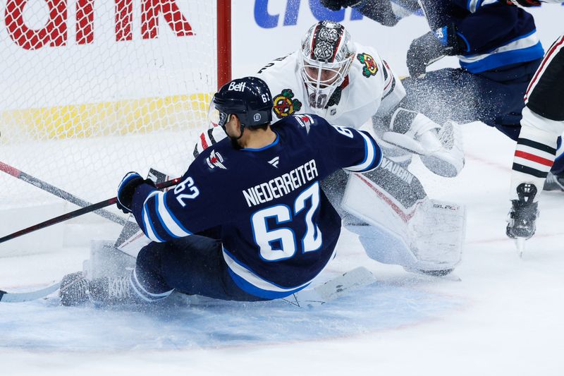 Oct 11, 2024; Winnipeg, Manitoba, CAN; Winnipeg Jets forward Nino Niederreiter (62) slides into Chicago Blackhawks goalie Arvid Soderblom (40) during the third period at Canada Life Centre. Mandatory Credit: Terrence Lee-Imagn Images