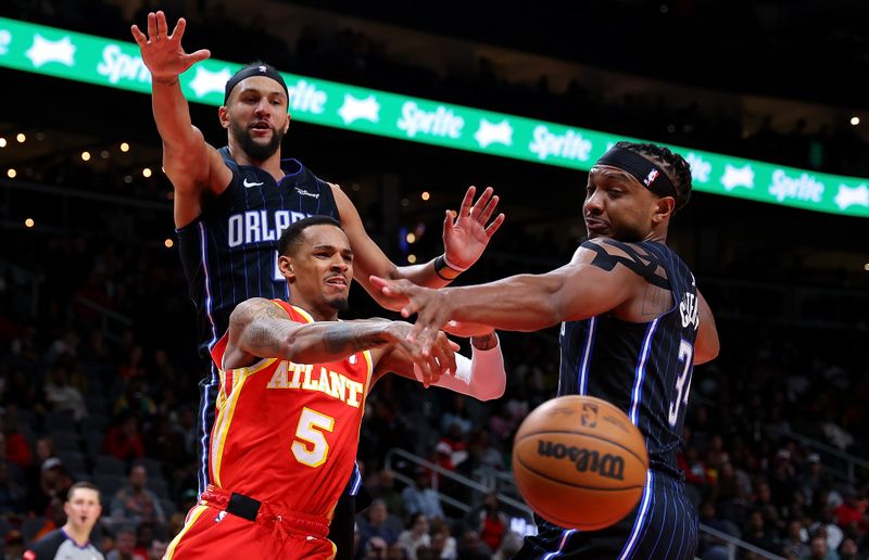 ATLANTA, GEORGIA - FEBRUARY 25:  Dejounte Murray #5 of the Atlanta Hawks passes the ball as he drives against Jalen Suggs #4 and Wendell Carter Jr. #34 of the Orlando Magic during the fourth quarter at State Farm Arena on February 25, 2024 in Atlanta, Georgia.  NOTE TO USER: User expressly acknowledges and agrees that, by downloading and/or using this photograph, user is consenting to the terms and conditions of the Getty Images License Agreement.  (Photo by Kevin C. Cox/Getty Images)