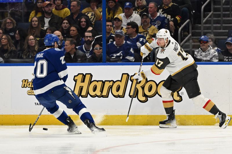 Dec 21, 2023; Tampa, Florida, USA; Las Vegas Golden Knights defensemen Ben Hutton (17) passes the puck past Tampa Bay Lightning left wing Nicholas Paul (20) in the third period at Amalie Arena. Mandatory Credit: Jonathan Dyer-USA TODAY Sports