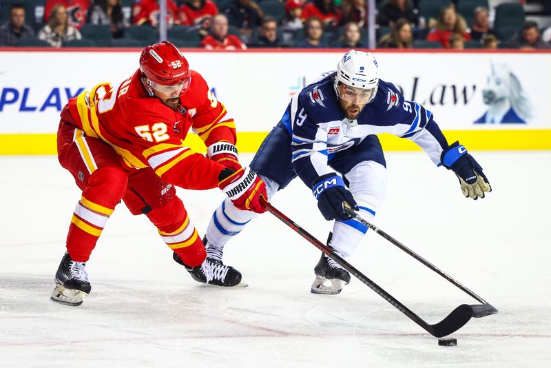 Oct 4, 2024; Calgary, Alberta, CAN; Calgary Flames defenseman MacKenzie Weegar (52) and Winnipeg Jets left wing Alex Iafallo (9) battles for the puck during the first period at Scotiabank Saddledome. Mandatory Credit: Sergei Belski-Imagn Images