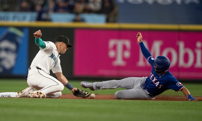 Jun 15, 2024; Seattle, Washington, USA; Texas Rangers second baseman Marcus Semien (2) steals second base as a throw gets away from Seattle Mariners second baseman Dylan Moore (25) during the first inning at T-Mobile Park. Mandatory Credit: Stephen Brashear-USA TODAY Sports