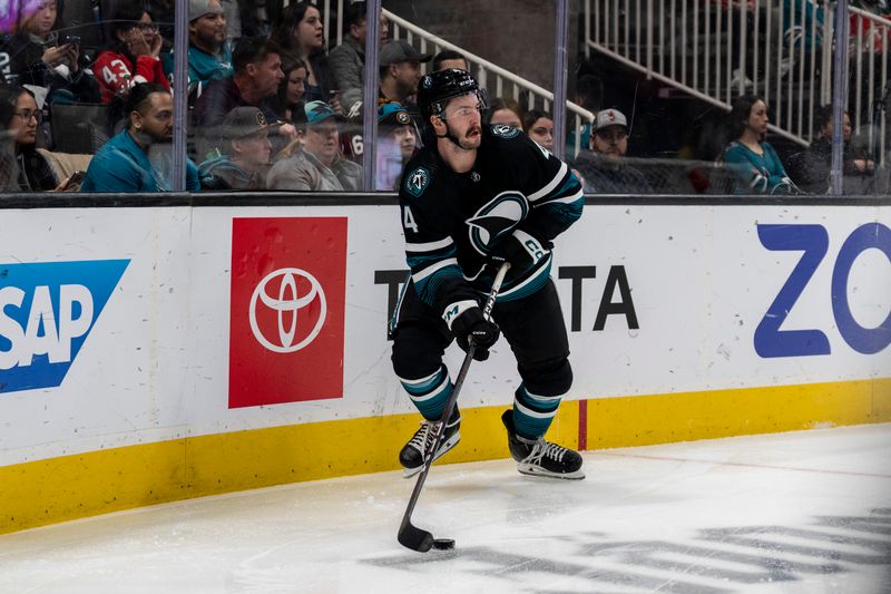 Feb 27, 2024; San Jose, California, USA;  San Jose Sharks defenseman Kyle Burroughs (4) skates with the puck behind the net against the New Jersey Devils during the first period at SAP Center at San Jose. Mandatory Credit: Neville E. Guard-USA TODAY Sports