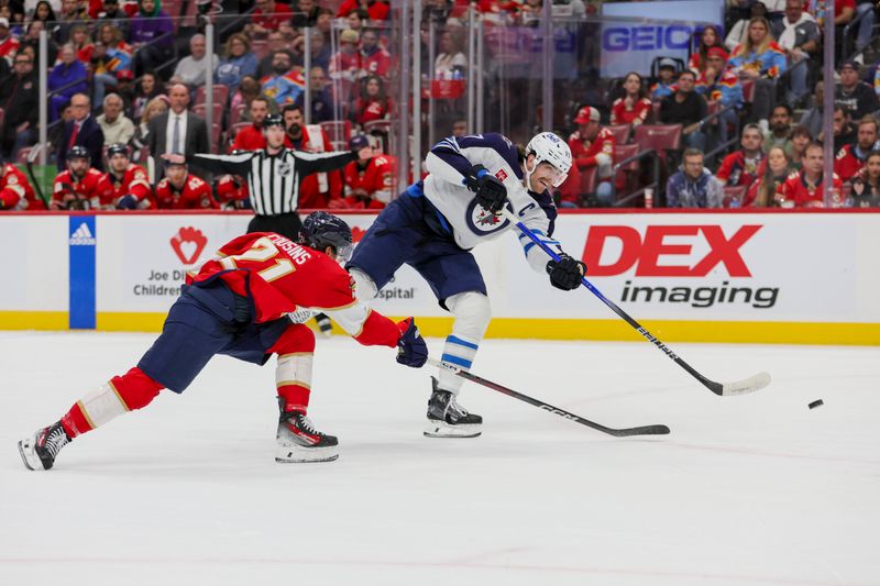 Nov 24, 2023; Sunrise, Florida, USA; Winnipeg Jets center Adam Lowry (17) shoots the puck as Florida Panthers center Nick Cousins (21) defends during the first period at Amerant Bank Arena. Mandatory Credit: Sam Navarro-USA TODAY Sports