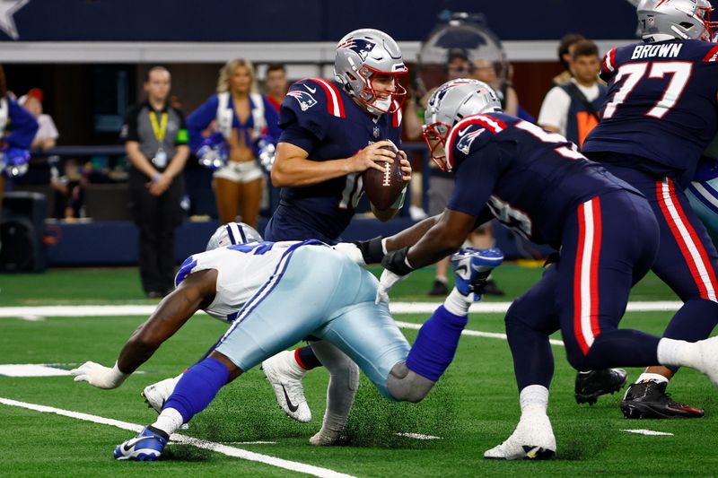 New England Patriots quarterback Mac Jones, center, avoids pressure by Dallas Cowboys defensive end DeMarcus Lawrence, bottom left, during the first half of an NFL football game in Arlington, Texas, Sunday, Oct. 1, 2023. (AP Photo/Roger Steinman)