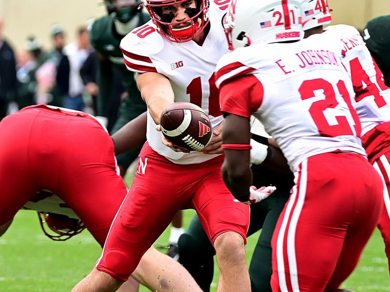 Nov 4, 2023; East Lansing, Michigan, USA;  Nebraska Cornhuskers quarterback Heinrich Haarberg (10) hands the ball to running back Emmett Johnson (21) against the Michigan State Spartans at Spartan Stadium. Mandatory Credit: Dale Young-USA TODAY Sports