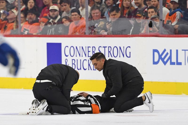 Nov 18, 2024; Philadelphia, Pennsylvania, USA; Referee Barry Anderson (20) is looked at by trainers after colliding with a player during game between Philadelphia Flyers and Colorado Avalanche in the first period at Wells Fargo Center. Mandatory Credit: Eric Hartline-Imagn Images